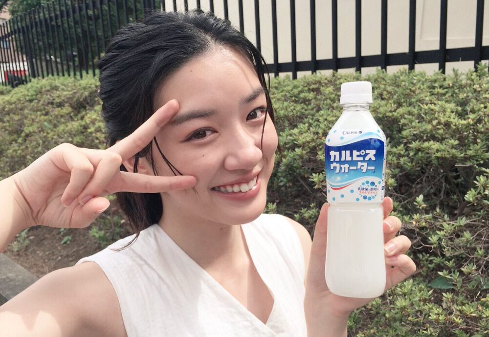 永野芽郁がカルピスを持ってピースする写真